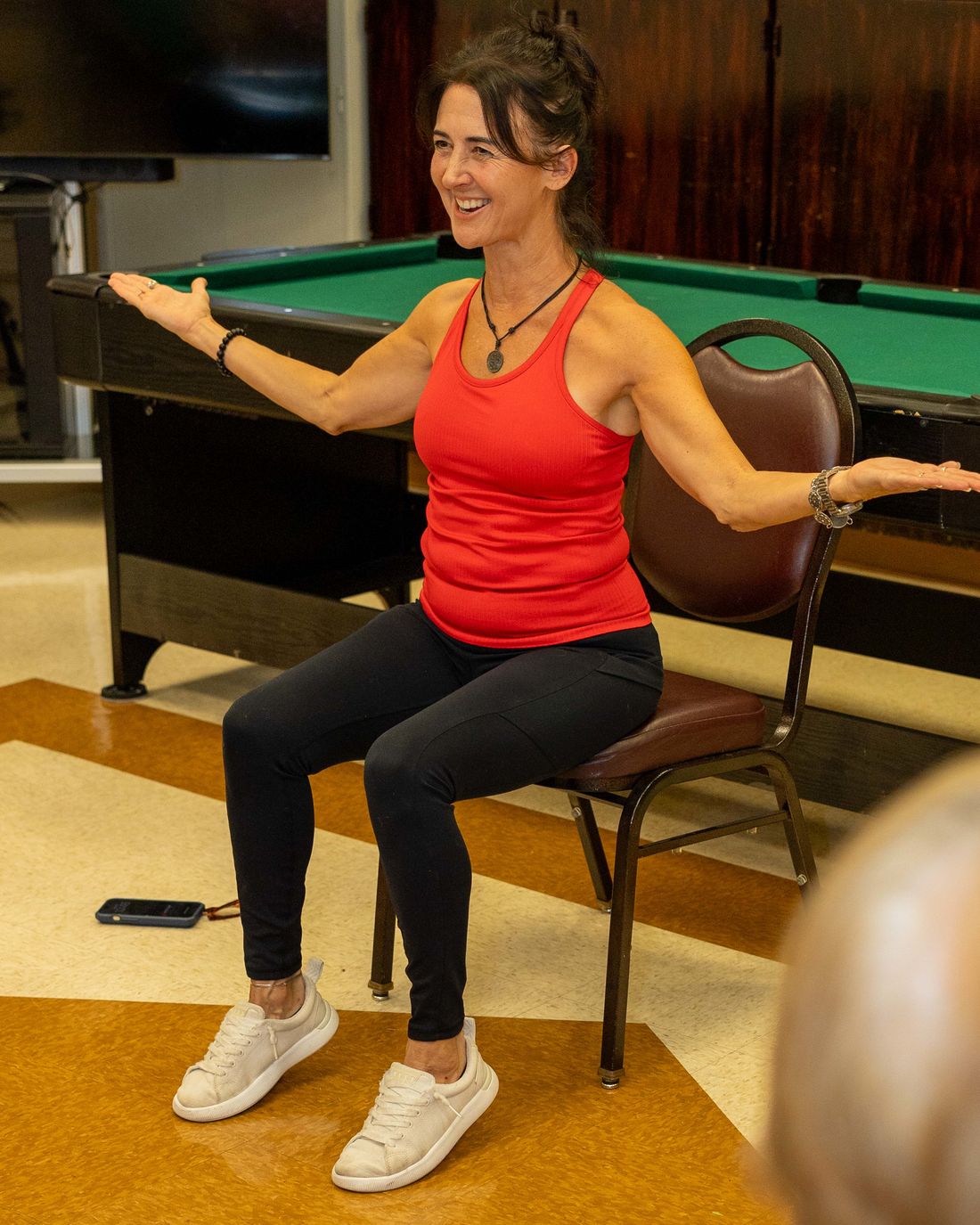 Nikki DeJulia seated on a chair with her arms open wide, smiling.