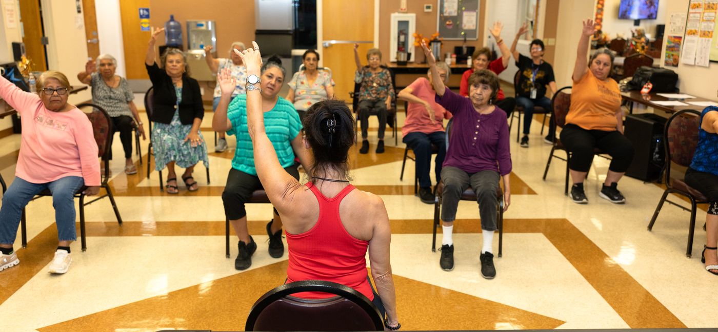 Nikki, seen from behind, leading a full room of chair fitness participants.