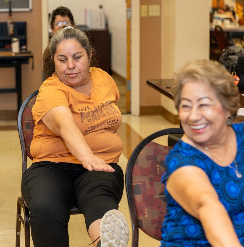 Two participants reach across their bodies in a seated twist, one laughing.